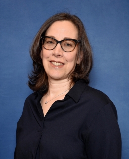 woman in a blue button-up blouse in glasses with medium-length hair smiles
