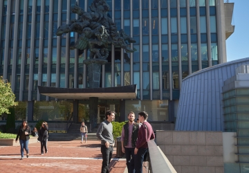 Three students talk on Revson Plaza next to the Pegasus statue