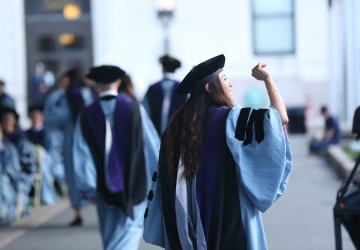 A female graduate waving and wearing regalia at Law School graduation.