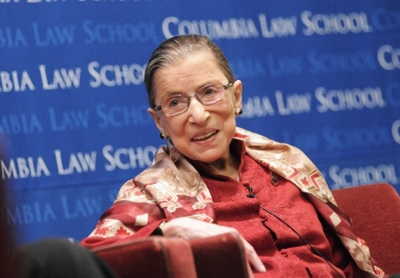 Ruth Bader Ginsburg smiles in front of a blue Columbia Law School backdrop