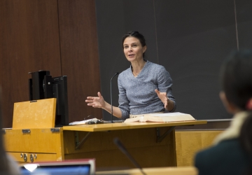  Professor Maeve Glass stands behind a lectern in a classroom at Columbia Law School/