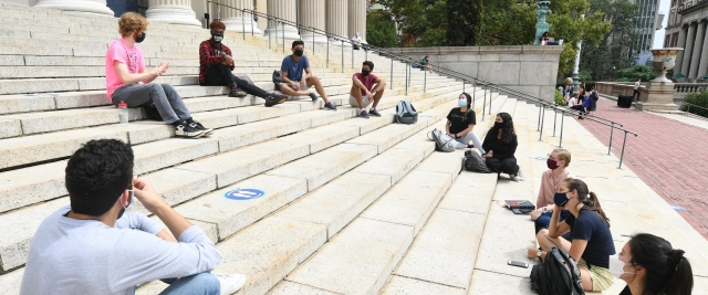 Students wearing masks sitting on the library steps, socially distanced