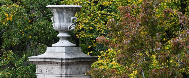 A stone urn on a pediment at the gates of Columbia with autumn leaves