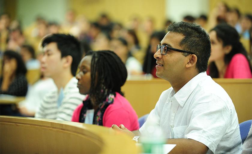 A student in a white shirt sits in a lecture hall and smiles.