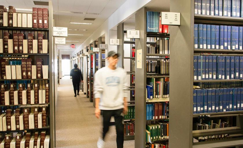 A student walks between stacks of books in the library
