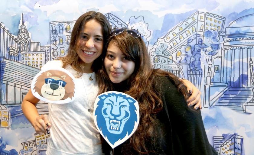 Two students hold Columbia lion logos in front of a watercolor Columbia backdrop on Giving Day