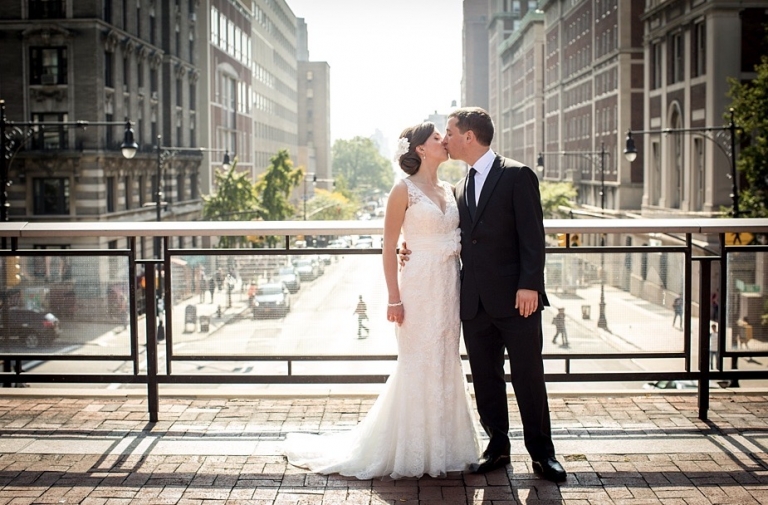   Casey Boyle in wedding dress and Nicholas Duston kissing on plaza overlooking Amsterdam Avenue