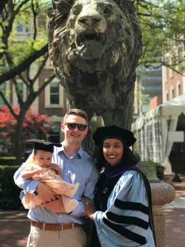 Man holding baby and woman in graduation gown and cap