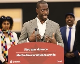 Man speaking in front of Stop Gun Violence sign