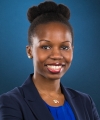 Pictured above is Temitope K. Yusuf. She is wearing a royal blue shirt under a navy blue blazer. She has pearl studs in each ear. She is smiling wide, and has wine colored rouge on her lips. She has dark brown eyes and curly hair tied back into a bun. 