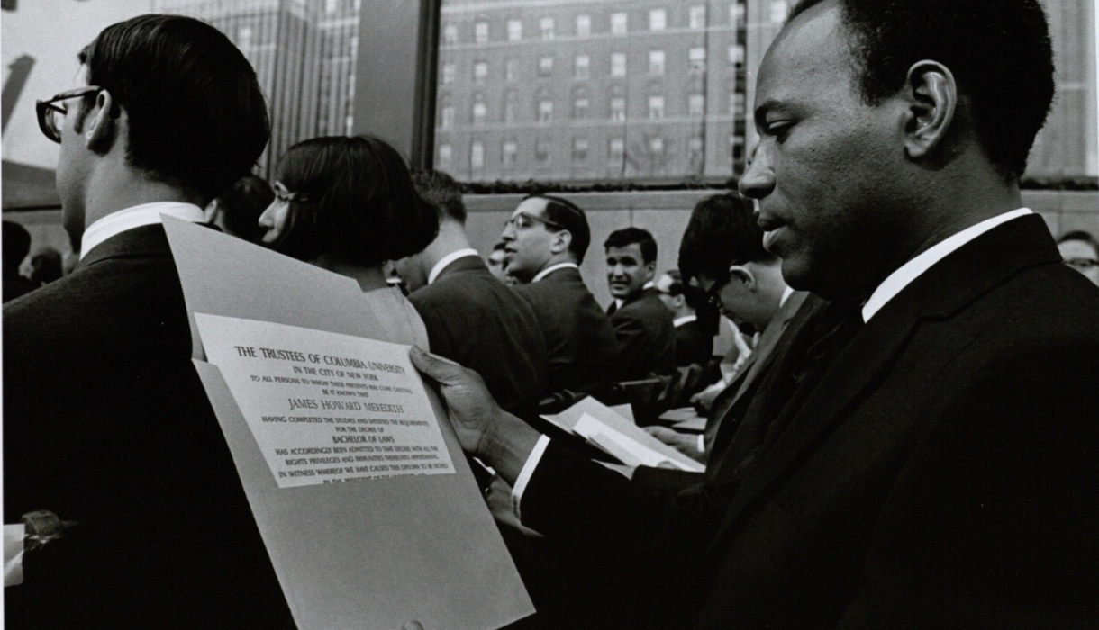 Seated James Meredith looks at diploma at graduation