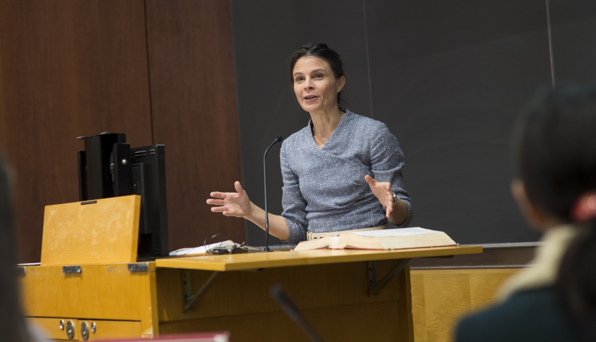 Professor Maeve Glass stands behind a lectern in a classroom at Columbia Law School/