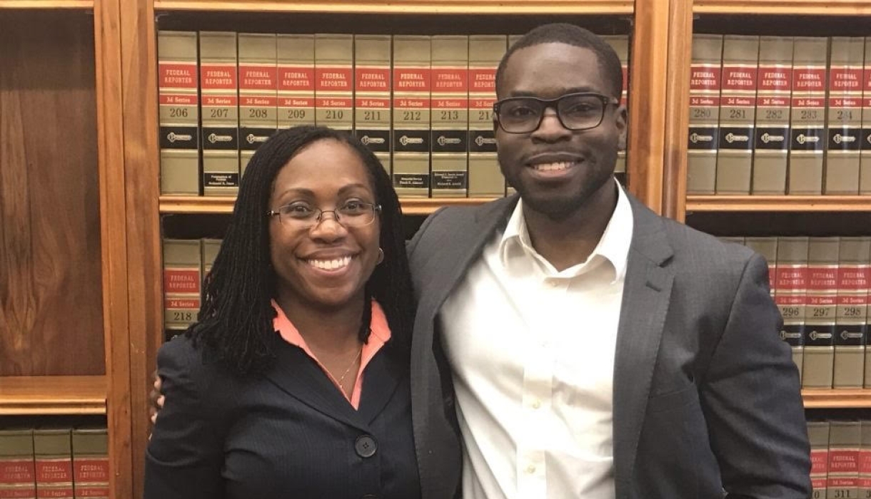 A woman and man both in dark suits, in front of law books 