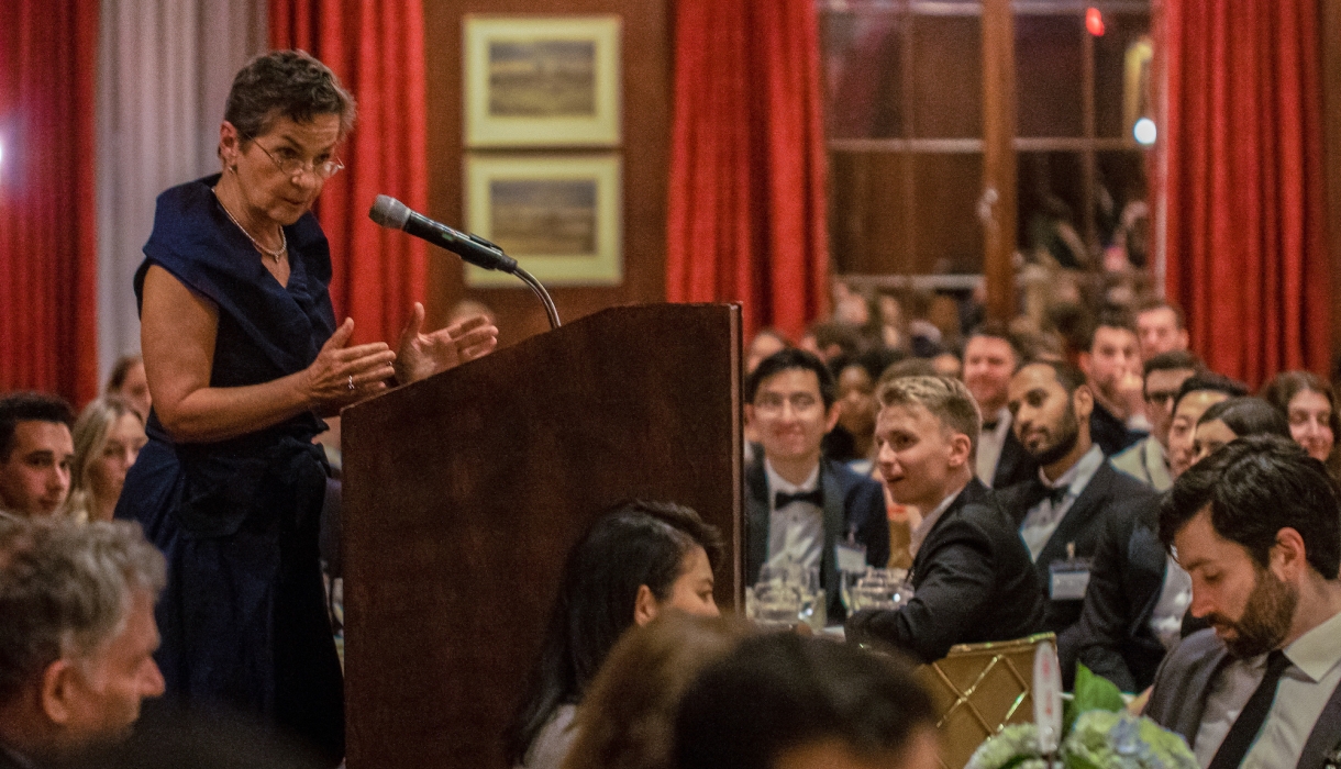 Woman in black dress at podium surrounded by students