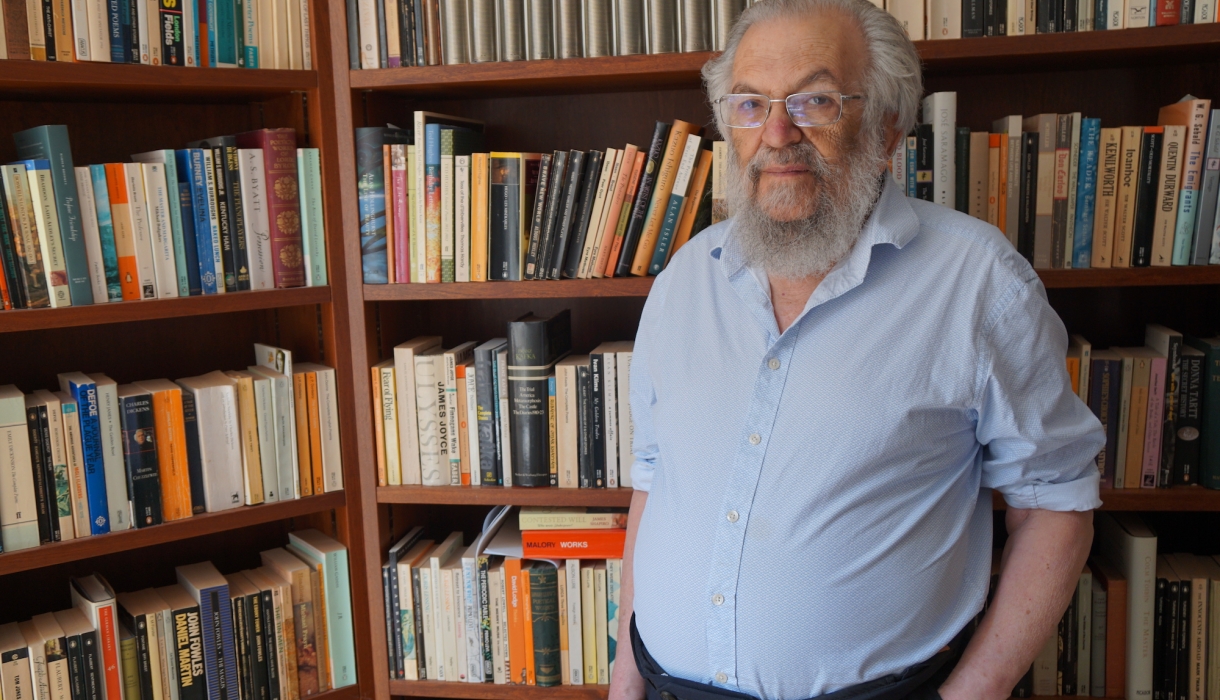 Man with  beard and shirtsleeves in front of bookcases