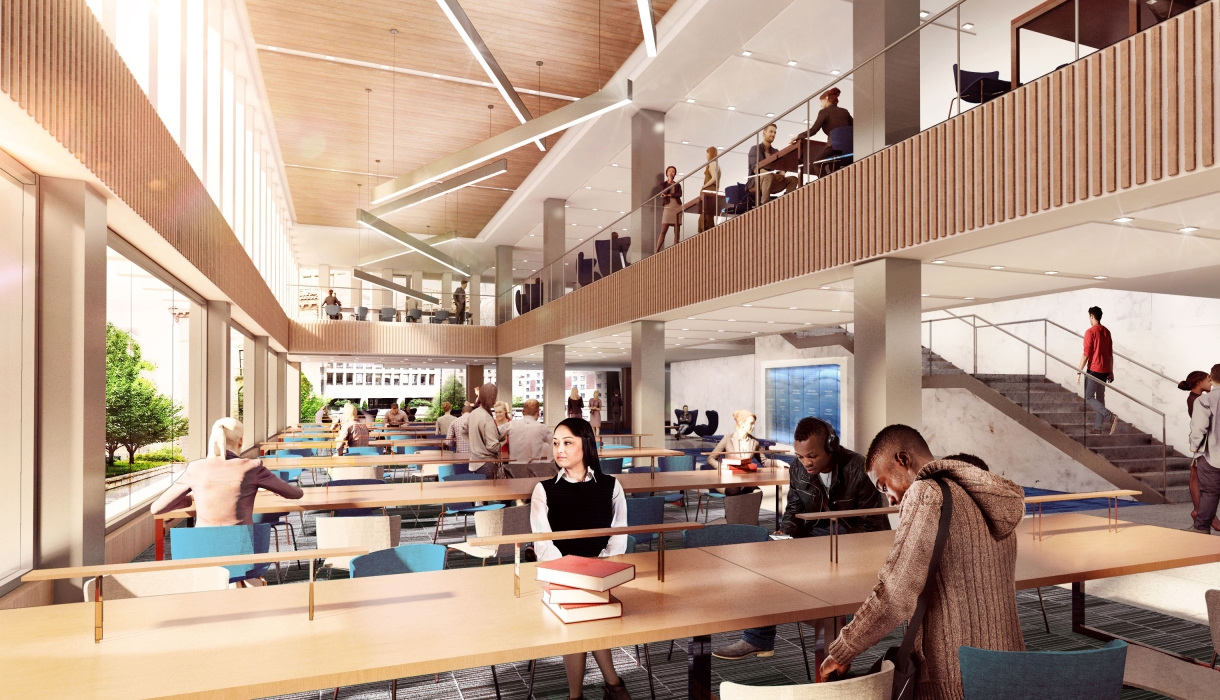 Students sit at long tables next to a bank of windows and beneath a mezzanine.