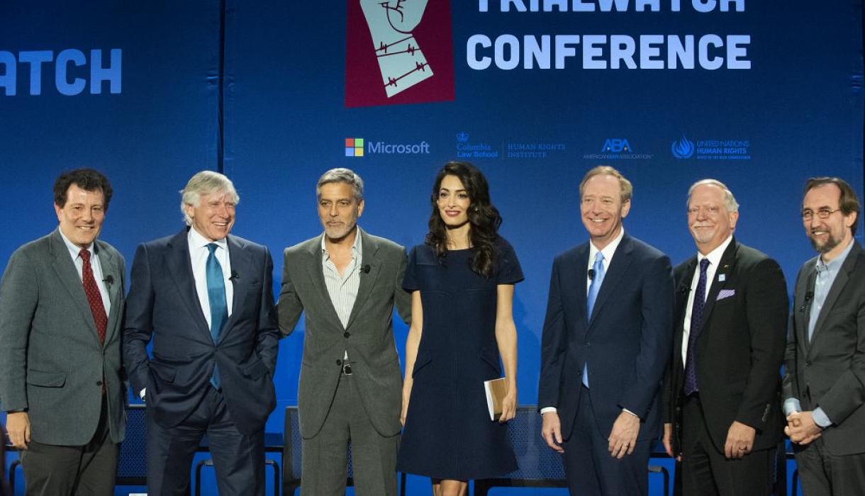 6 men in suits flank a woman in black dress