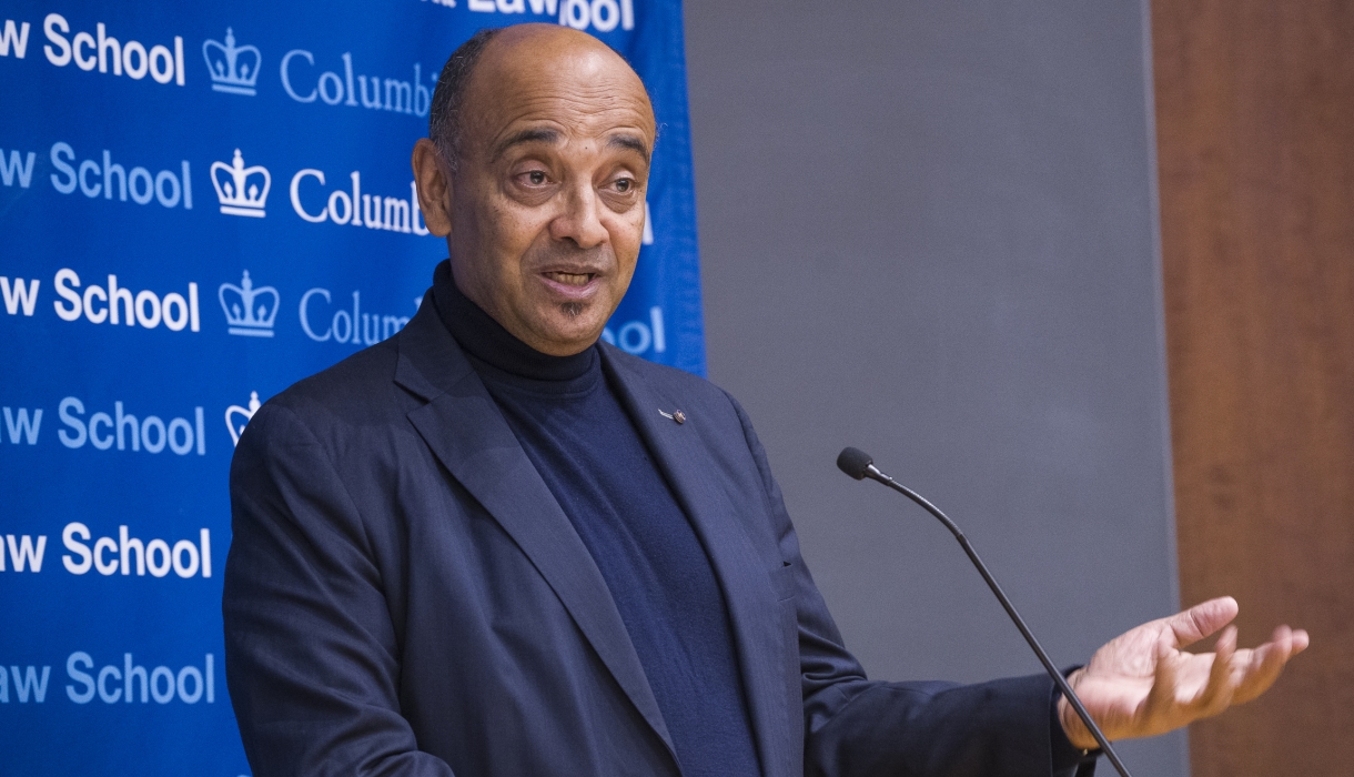 Man speaking at microphone gestures.