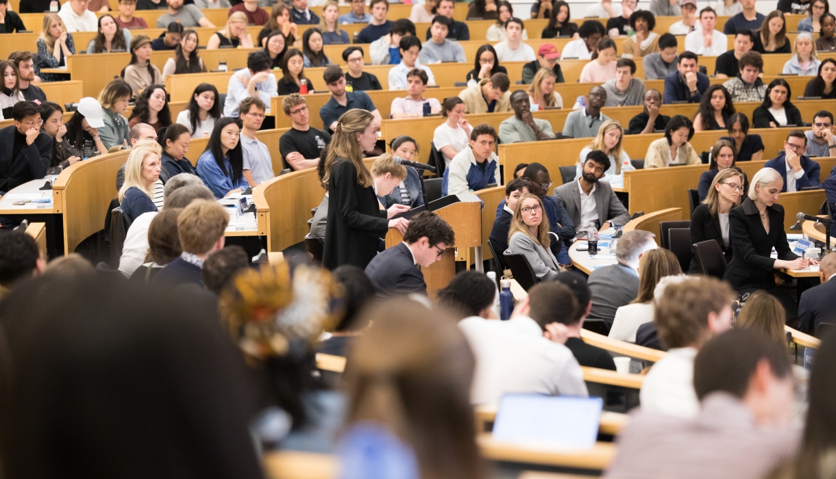 A student at the podium surrounded by fellow students, faculty, and family watching the 2026 Harlan Fiske Stone Moot Court finals.