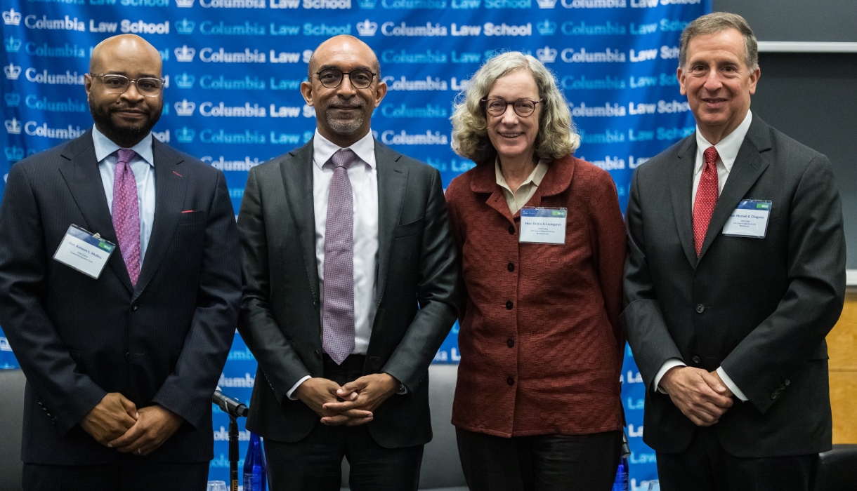 Justice Raheem L. Mullins in suit, Columbia Law Dean Daniel Abebe in suit and tie, Judge Debra Livingston in brick-colored jacket, and Judge Michael A. Chagares in suit and tie all standing in front of a Columbia Law School banner