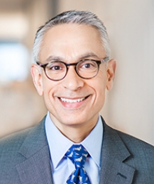 Gray-haired man with horn-rimmed glasses in gray suit and blue tie