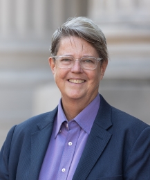 Image of Katherine Franke, wearing glasses, a purple button-up shirt and a navy blue blazer