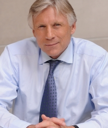 President Lee Bollinger smiles while folding his hands on a desk in front of him.