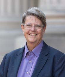 Image of Katherine Franke, wearing glasses, a purple button-up shirt and a navy blue blazer
