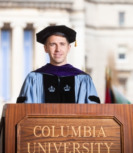 Brown haired man in academic cap and gown behind podium
