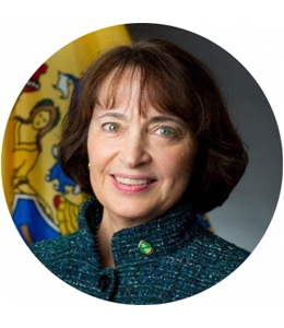 Portrait of woman with brown hair in green jacket in front of New Jersey state flag