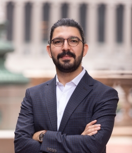 Man with glasses and a beard in a blue jacket and white shirt