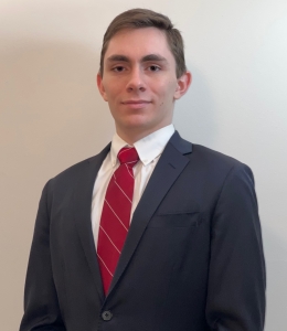 Student in gray suit and red tie stands in front of a white wall