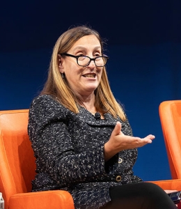 Woman with glasses speaking seated in a chair onstage