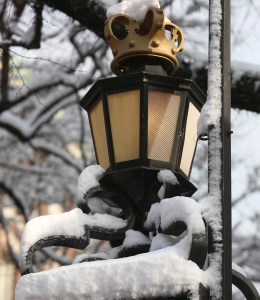 The crown-shaped finial of a wrought iron fence is covered in snow.