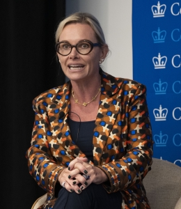 Blonde woman in glasses and patterned jacket speaking 