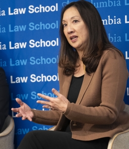 Dark-haired woman in brown jacket speaking