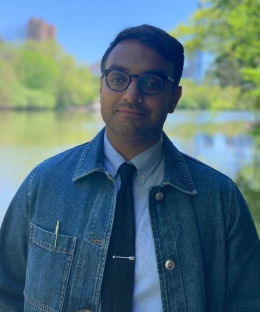 Man wearing glasses, a denim jacket, white shirt, and dark tie