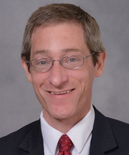 Headshot of a man wearing glasses, a white shirt, black blazer, and red tie