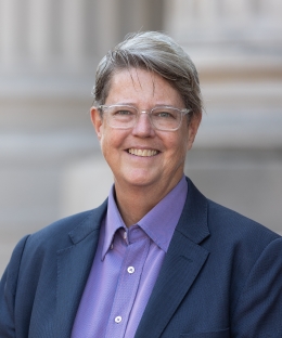 Image of Katherine Franke, wearing glasses, a purple button-up shirt and a navy blue blazer