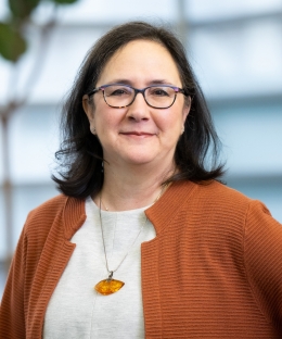 Liliana Vaamonde, smiling and wearing an orange cardigan and glasses