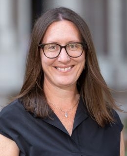 Jill Marden Casal wears a dark blue dress and brown glasses