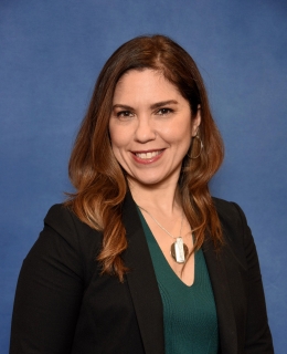 woman with medium length brown hair with a green shirt and black blazer smiles