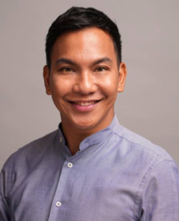Headshot of a man wearing a gray button up smiling at the camera