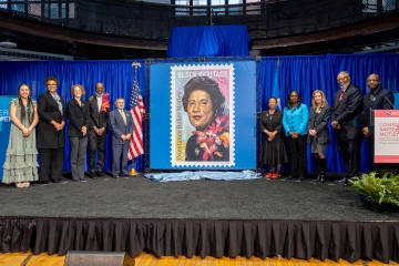 People stand on a stage on either side of a poster of Judge Constance Baker Motley