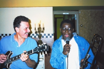 Vintage snapshot of man playing electric guitar next to man holding trombone and singing into a microphone