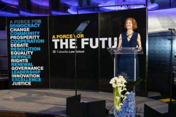 Woman at podium with signage behind her