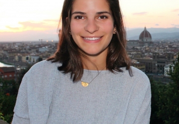 Columbia Law School graduate Emma DiNapoli ’20 in a pale gray sweater with clouds behind her