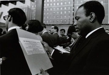 Seated James Meredith looks at diploma at graduation