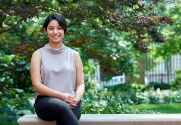 Bhagwati Fellow Sparsha Janardhan sits on a bench outside Jerome Greene Hall