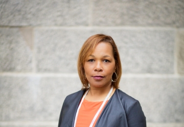 Woman in orange dress, pearls and gray jacket